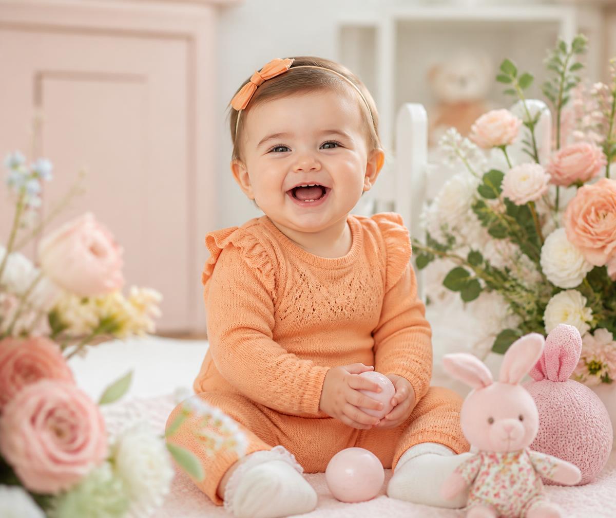 Smiling baby in a soft orange knit outfit surrounded by pastel flowers
